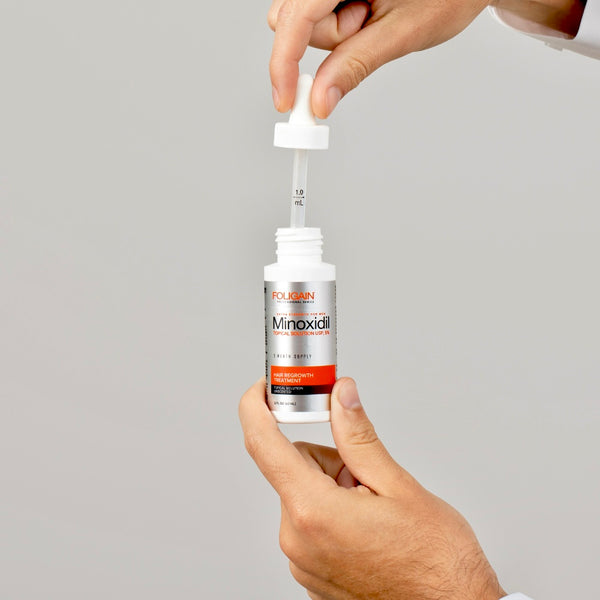 Foligain Minoxidil bottle with dropper held by a hand against a gray background